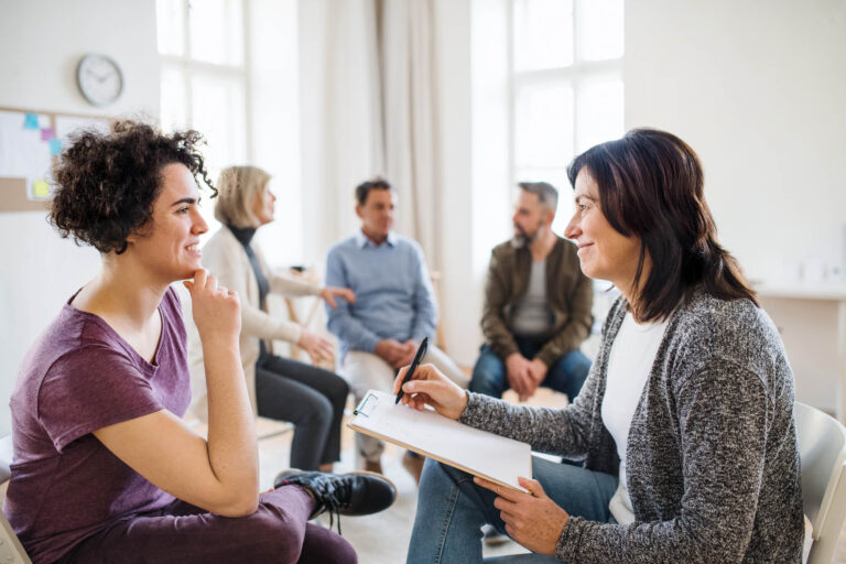 Solentra Wellness | Senior counsellor with clipboard talking to a woman during group therapy.