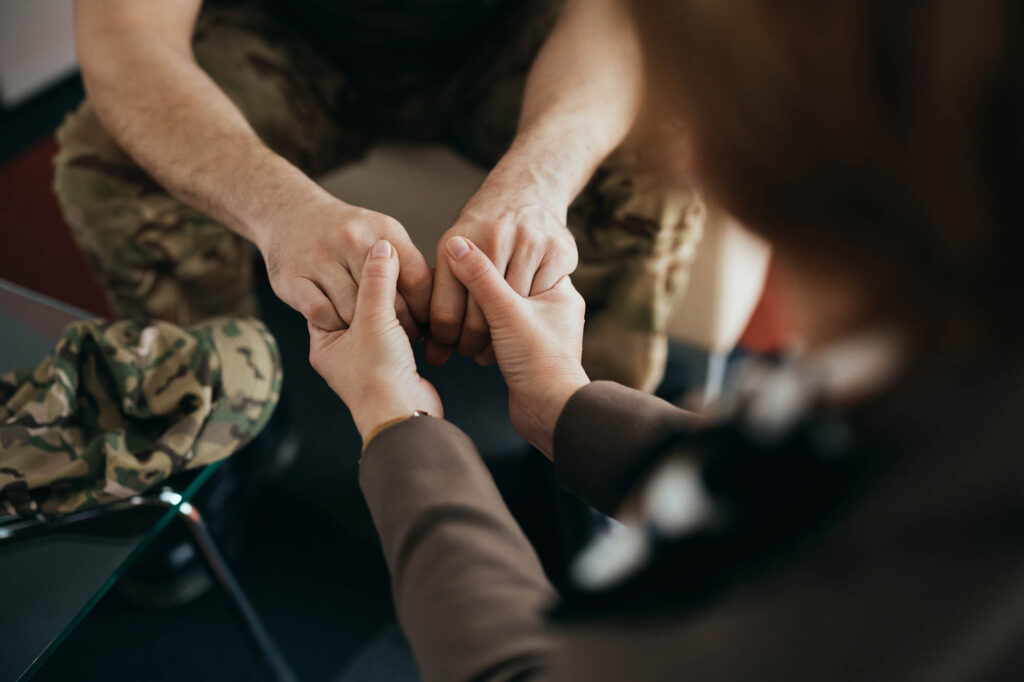 Solentra Wellness | Close-up of psychotherapist holding hands with a soldier during counseling at her office.